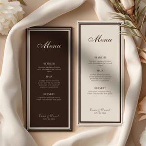 Op de afbeelding: Twee elegante trouwmenu's met een zwart-wit ontwerp. De menu's bevatten een driegangenmaaltijd met voorgerecht, hoofdgerecht en dessertopties. De namen Emma & Daniel en de datum staan onderaan.