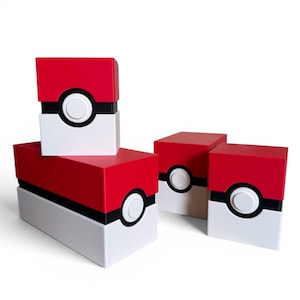 Op de afbeelding: Verschillende rode, witte en zwarte dozen die op Poké Balls lijken, zijn gestapeld en gerangschikt op een witte achtergrond. De dozen hebben een rode bovenkant, een witte onderkant en een zwarte band met een witte cirkel in het midden. De dozen zijn een populair item.