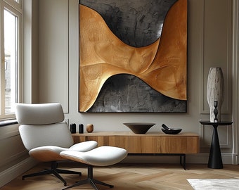 Op de afbeelding: Een modern woonkamerinterieur met een hedendaags abstract schilderij in goud en zwart. Het schilderij hangt boven een houten mediaconsole met een witte fauteuil en een voetenbank.