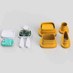 Op de afbeelding: Een set gele plastic koekjesvormen in de vorm van een persoon, een rechthoek, een ovaal en een cirkel. De vormen liggen op een wit oppervlak.