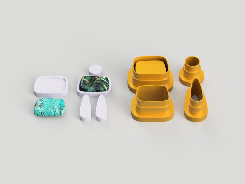 Op de afbeelding: Een set gele plastic koekjesvormen in de vorm van een persoon, een rechthoek, een ovaal en een cirkel. De vormen liggen op een wit oppervlak.