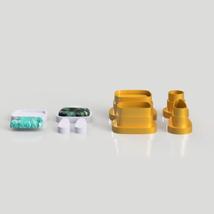 Op de afbeelding: Een set van vijf gele plastic koekjesvormen in verschillende vormen, waaronder een rechthoek, een cirkel en een hart. De vormen zijn gerangschikt op een wit oppervlak.