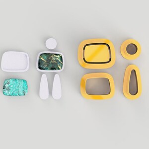 Op de afbeelding: Een set witte en gele geometrische vormen met een groene en blauwe steen in het midden. De vormen zijn gerangschikt in een patroon dat lijkt op een persoon.