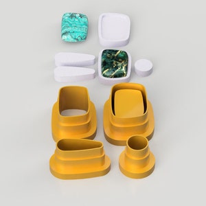 Op de afbeelding: Een set van zeven gele plastic koekjesvormen in verschillende vormen, waaronder een rechthoek, een ovaal en een cirkel. De vormen zijn op elkaar gestapeld.