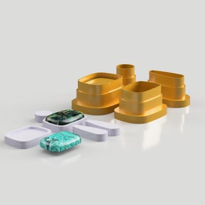 Op de afbeelding: Een set van vijf gele plastic koekjesvormen in de vorm van een persoon. De vormen zijn op elkaar gestapeld. In het midden van de afbeelding is een groene en zwarte steen.