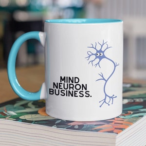 Op de afbeelding: Een witte keramische mok met een blauwe handgreep en een blauwe neuron afbeelding. De mok heeft de tekst "Mind Neuron Business." erop gedrukt.