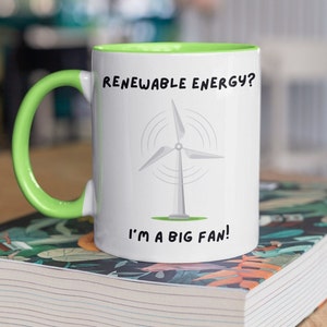May include: White ceramic mug with a green rim and handle. The mug features a black and white illustration of a wind turbine with the text "Renewable Energy? I'm a big fan!"