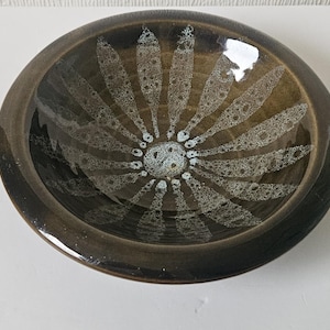 以下が含まれることがあります： 白とグレーの花柄が施された茶色の陶器のボウル。ボウルは光沢のある仕上げで、縁がわずかに盛り上がっています。