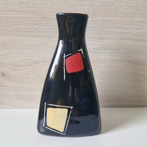 May include: A black ceramic vase with a flared base and narrow neck. The vase features a red square and a yellow square with white outlines. The vase is approximately 20 cm tall.