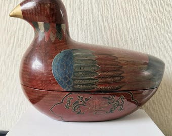 May include: A red wooden duck shaped box with intricate painted details. The duck has a gold beak and blue, green, and red painted feathers. The box is decorated with a floral design on the bottom.