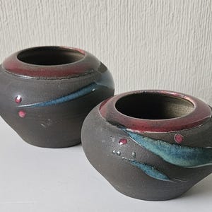 May include: Two dark brown ceramic pots with red and blue glaze. The larger pot has a blue and red design, while the smaller pot has a blue and red design with a more abstract pattern.
