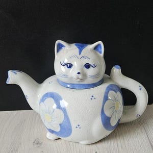 Puede incluir: Una taza de cerámica blanca con un asa negra y el texto "But First, Coffee" en negrita negra. La taza se encuentra sobre un fondo neutro, resaltando su diseño simple.