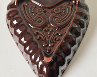 May include: A brown heart-shaped ceramic baking dish with a raised design of two birds and a floral pattern.
