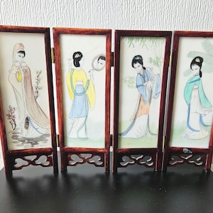 May include: A four-panel folding screen with watercolour illustrations of women in traditional Asian dress. The dark reddish-brown wooden frames enclose artwork depicting figures in various poses and colourful garments. The screen is designed to stand upright.