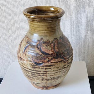 May include: A brown and beige ceramic vase with a textured surface and a wide mouth. The vase has a unique design with brown and beige swirls and lines.