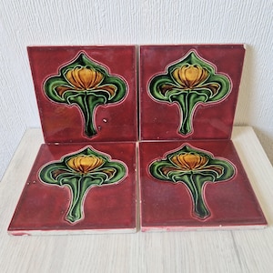 May include: Four square ceramic tiles with a floral design. Each tile features a stylized flower with yellow, green, and brown accents on a deep red background.