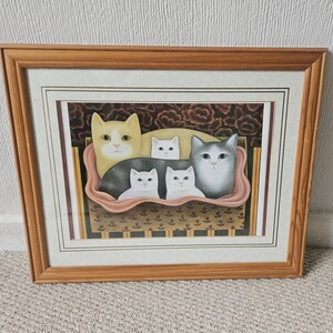 May include: A framed print featuring a group of five cats in a pink basket. The cats include one large yellow cat, one large gray cat, and three smaller white cats. The background shows a dark floral pattern and a striped border in a wooden frame.