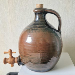May include: A brown and black ceramic jug with a wooden spigot and cork stopper. The jug has a rounded body and a handle.