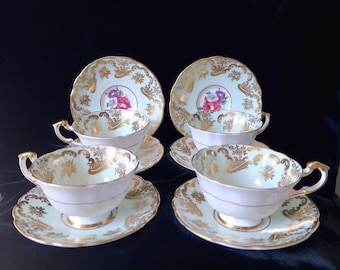 May include: Set of four teacups and saucers with a delicate floral design and gold accents. The cups and saucers are a pale green color with a white interior.