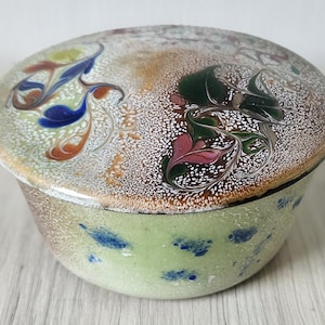 May include: A ceramic trinket box with a lid. The box is decorated with a marbled design in shades of green, blue, pink, and brown. The lid has a white background with a marbled design in shades of green, blue, pink, and brown.