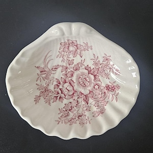 May include: White ceramic seashell-shaped dish with a ruffled edge. The dish features a floral and bird design in shades of red. The decorative dish is suitable for serving or display.
