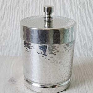 May include: Silver hammered metal container with a lid. The container has a smooth, rounded bottom and a slightly raised rim around the top.