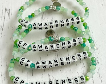 May include: Four beaded bracelets with green and white beads. Each bracelet has white letter beads spelling "CP AWARENESS". The bracelets have a silver charm that says "Bracelet Therapy".
