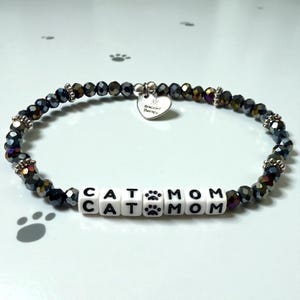 May include: A white ceramic mug with a black handle and the text "But First, Coffee" in a bold, black font. The mug is sitting on a wooden surface. The mug is approximately 4 inches tall.