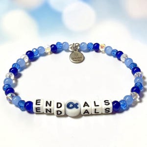 May include: A blue beaded bracelet with the words "END ALS" spelled out in white letter beads. The bracelet includes a charm that says "Bracelet Therapy". The beads are various shades of blue and clear.