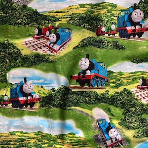 May include: Fabric featuring a repeating pattern of the blue Thomas the Tank Engine train, along with other train characters, set against a backdrop of green hills, trees, and blue skies. The design includes train tracks.