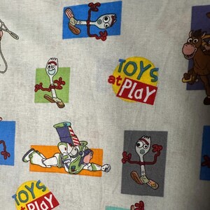 K&ouml;nnte beinhalten: Stoff mit einem sich wiederholenden Muster von Charakteren aus dem Film Toy Story. Das Design umfasst Bilder von Forky, Buzz Lightyear und einem Pferd sowie den Text "TOYS at PLAY" in einem roten und gelben Kreis.