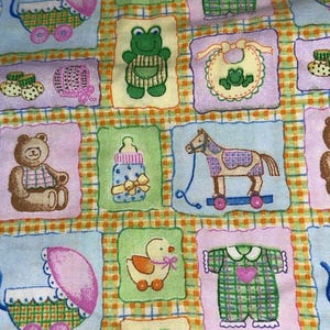 May include: A patchwork fabric featuring baby-themed illustrations. The design includes squares with images of a baby carriage, a teddy bear, a rocking horse, a duck, a frog, a baby bottle, and baby clothes. The color palette is pastel with a plaid background.