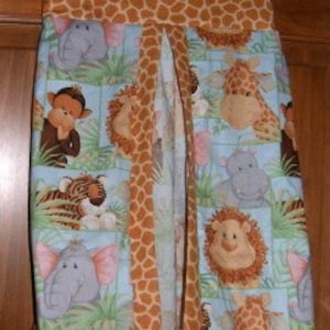 Pode incluir: Um organizador de fraldas com estampa de girafa, elefante e macaco. O organizador é feito de tecido marrom e azul com uma estampa de girafa marrom e branca na frente. O organizador tem um bolso na frente e um laço para pendurar na parte superior.