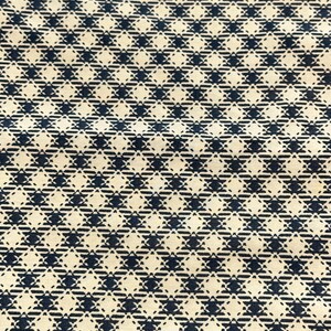 May include: Close-up of a fabric with a repeating pattern. The pattern features navy blue star-like shapes on a cream-colored background. The design is made up of solid and dashed lines, creating a textured appearance. The fabric appears to be cotton or a similar material.