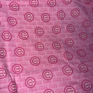 May include: Pink fabric with a repeating pattern of the Chicago Cubs logo and the word "CUBS" in white. The design features the team's logo and name.