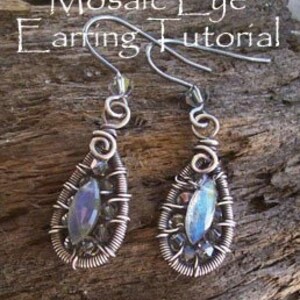 May include: A pair of handmade wire-wrapped earrings with a teardrop shape. Each earring features a central iridescent stone, surrounded by intricate wirework and small beads. The text "Mosaic Eye Earring Tutorial" and "Delia Stone" are visible.