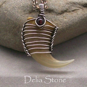 Peut inclure: Un pendentif en griffe enveloppé de fil d'argent avec une pierre précieuse rouge foncé. Le pendentif est suspendu à une chaîne en argent.