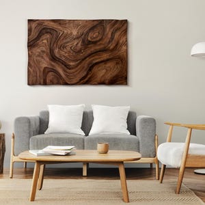 May include: A living room interior design with a gray sofa, two white throw pillows, a wooden coffee table, a white armchair, a wooden side table, a potted plant, and a large wall art featuring a brown wood grain pattern.