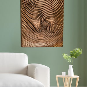 May include: A rectangular wooden wall art piece with a carved, concentric circular design. The artwork is a warm brown color and hangs on a green wall. A white sofa and small table with a vase are in the foreground.
