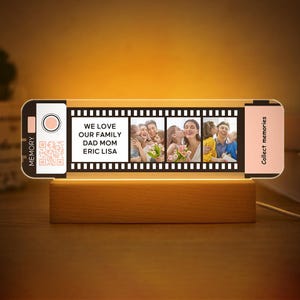 May include: A personalised photo night light with a wooden base. The light features a film strip design with family photos and the text "WE LOVE OUR FAMILY DAD MOM ERIC LISA". The light also has the text "Collect memories".