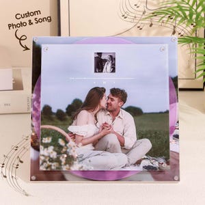 May include: A personalized photo and song print featuring a couple kissing, set against a field backdrop. The print includes a small photo, a music player graphic, and the text "Custom Photo & Song". The background has a purple vinyl record design.