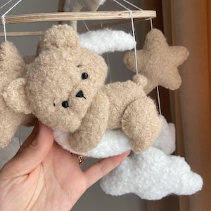 May include: A baby mobile with a brown teddy bear, white clouds, and brown stars hanging from a wooden ring.