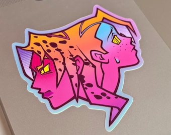 Op de afbeelding: Een gestanste sticker met een illustratie van twee gezichten in dubbel profiel, rug aan rug geplaatst. Het ontwerp gebruikt een levendig verloop van oranje, roze en paars met zwarte vlekken, gele ogen en een paars halftoon-stippenpatroon.