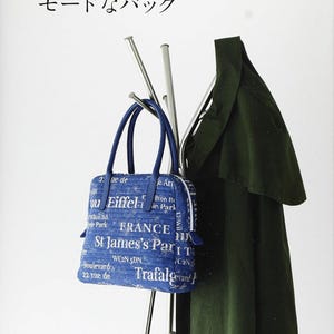 May include: A blue handbag with a white print of various European cities and landmarks. The bag is hanging on a silver coat rack with a green coat hanging on the rack.