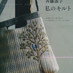 May include: A quilted tote bag with a tree design. The bag is light-colored with a textured pattern and a tree embroidered on the front. The tree has green leaves and a blue bird. Text in Japanese is visible.