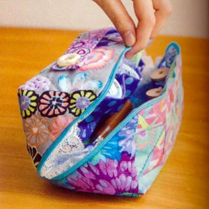 May include: A colorful fabric zippered pouch with a floral pattern and a button closure. The pouch is open and filled with various items, including spools of thread and a small bottle.