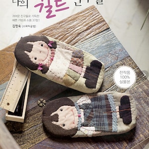May include: Two patchwork fabric doll pencil cases. The dolls have brown hair, brown eyes, and are wearing colorful clothing. The text on the cover of the book says "My Utopia 22".