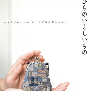 May include: A small, patchwork fabric coin purse with a silver clasp and a blue cord. The purse is held in the hands of a person.