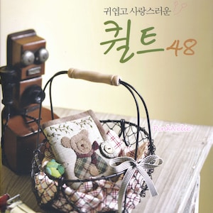 May include: A wire basket with a brown and white plaid fabric lining and a brown teddy bear fabric square inside. The basket has a wooden handle and a white bow. The text "PinkNelie" is visible in the image. The text "My Utopia : 6" is visible in the upper left corner of the image. The text "귀엽고 사랑스러운" is visible in the upper right corner of the image. The text "컷_48" is visible in the center of the image.