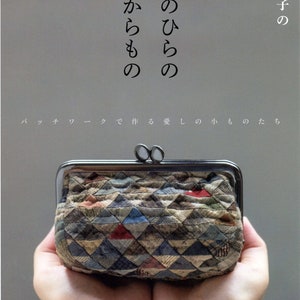 May include: A small, patchwork fabric purse with a silver clasp. The purse is held in two hands, with the background a light gray.